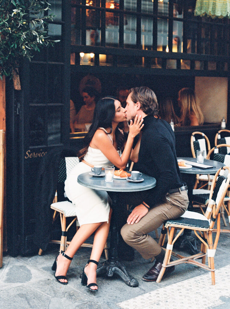 An engaged couple kissing at a Parisian cafe