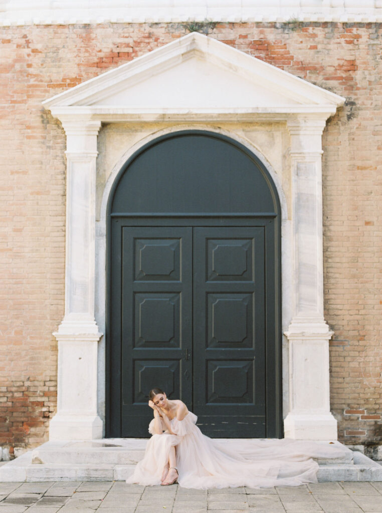 A woman sitting on stairs in front a long door in Venice